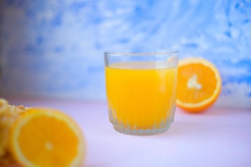 orange juice in glass with orange half on blue painted background