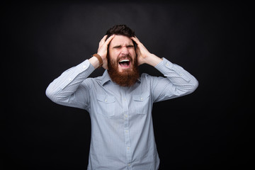 Handsome frustrated bearded man with hands on head and screaming over dark isolatd background