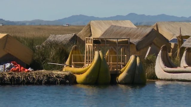 Medium spanning low-angle shot of floating village houses and traditional reed boats at Uros Island, Lake Titicaca, Peru