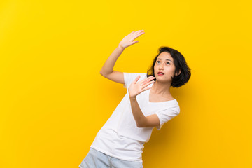 Asian young woman over isolated yellow wall nervous and scared