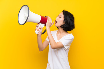 Asian young woman over isolated yellow wall shouting through a megaphone