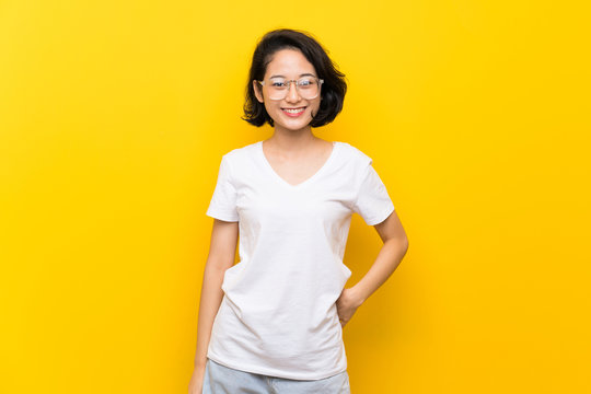 Asian Young Woman Over Isolated Yellow Wall With Glasses And Happy