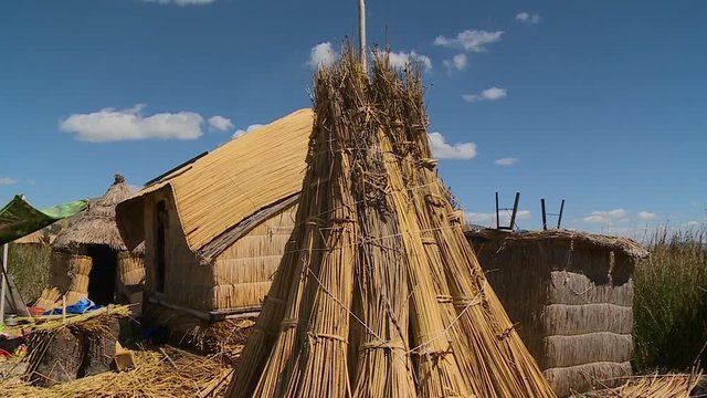 Close-up low angle tilting shot of a stack of dry totora reeds close to a traditional uros reed hut on a floating island, Lake Titicaca, Peru
