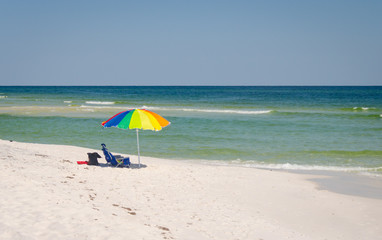 Umbrella and chairs set up at beach shoreline. Beautiful tropical Gulf Coast ocean beach white sands and sea. Vacation tourist travel destination for fun and relaxation.