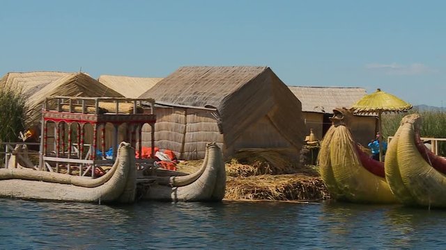 Medium low angle panning shot of uros floating village with anchored traditional totora boats, local reed houses, and villagers, Lake Titicaca, Peru