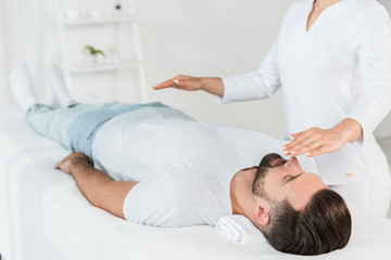 cropped view of healer with hands above body of man resting on massage table