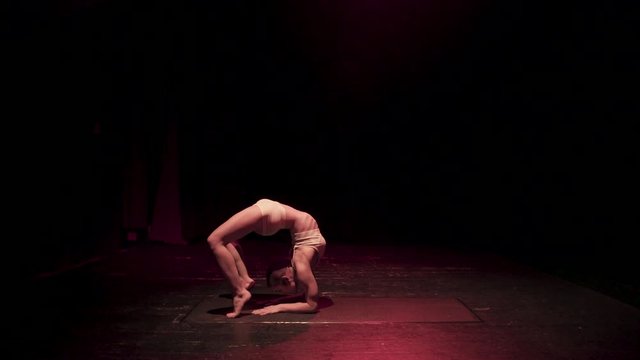 Female contortionist circus performer performing routine in dark studio