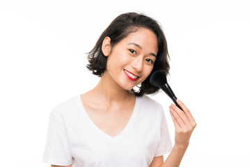 Asian young woman over isolated background with makeup brush