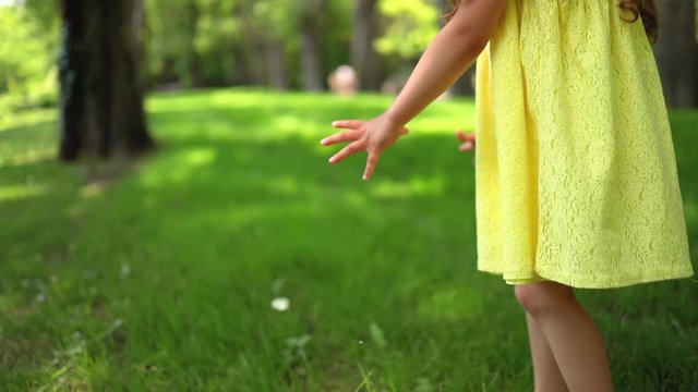 Happy little girl with yellow dress running barefoot on green grass in the park and try to catch a flying butterfly