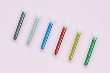 Colorful glitters lies on pastel pink background. Many long bottles with multi-colored bright sparkles for nail polish