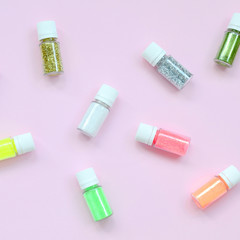 A flat lay pattern with colorful glitter bottles lies on pastel pink background