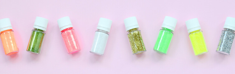 Colorful glitters lies on pastel pink background. Many round jars with multi-colored bright sparkles for nail polish