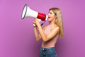 Teenager girl over isolated purple background shouting through a megaphone