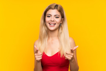 Teenager girl over isolated yellow background points finger at you
