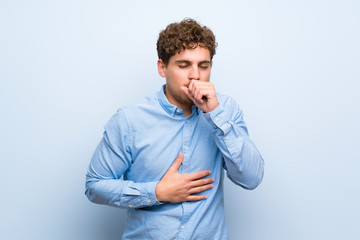 Blonde man over blue wall is suffering with cough and feeling bad