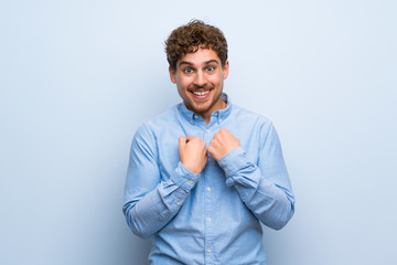 Blonde man over blue wall with surprise facial expression