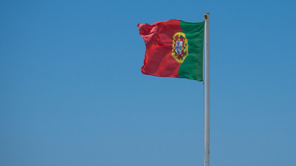 Portuguese flag against blue sky with space on left