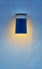 The blue lamp shines with warm light on the white wall.