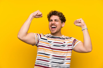 Blonde man over yellow wall celebrating a victory