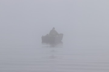 Fototapeta na wymiar Fisherman in the paddle boat in dense fog.