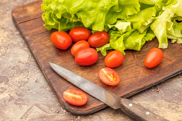 Cutting vegetables. Green lettuce and cherry tomatoes on an old cutting board. Cooking Diet food