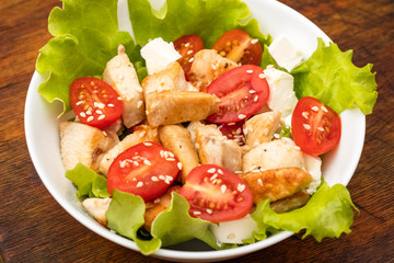 plate of Salad with chicken, tomatoes and soft cheese cheese. dressing with olive oil and sesame seeds. Dietary food. Wooden background