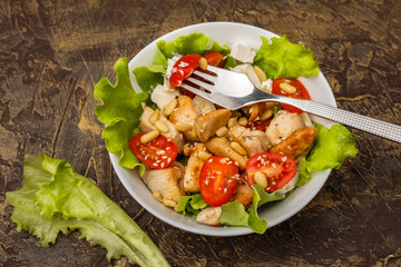 Warm salad with chicken, cherry tomatoes and soft cheese cheese, decorated with pine nuts. dressing with olive oil