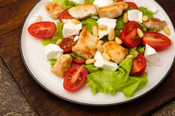 Salad with warm chicken, cherry tomatoes and soft brynza cheese, decorated with pine nuts. dressing with olive oil. Plate with dish on old cutting board
