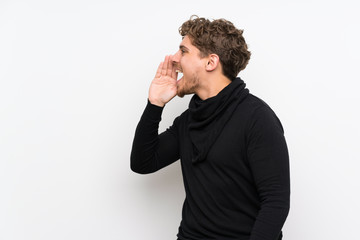 Blonde man over isolated white wall shouting with mouth wide open to the lateral