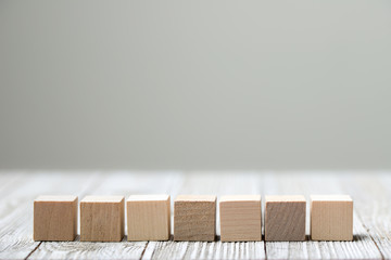 Seven wooden toy cubes arranged in row on white grey wooden background