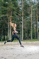 beautiful and sportive blonde woman running near green trees