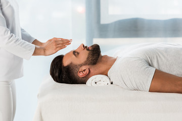 cropped view of healer putting hands above head of bearded man with closed eyes