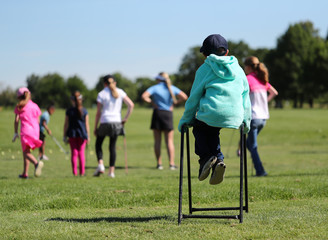 Fototapeta premium A little boy uses a golf bag stand to watch his sister practice golf