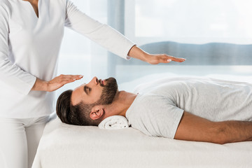 cropped view of healer putting hands above body of bearded man