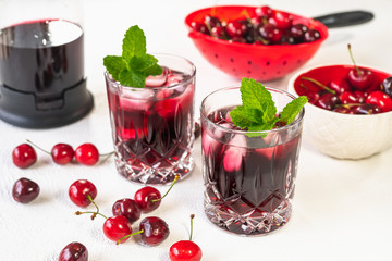 Fresh  Cold Cherry Juice in Glasses with Mint Leaves and Ice, and Cherries in a Bowl on White background Close Up