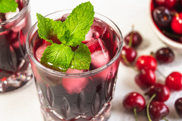 Fresh Cold Cherry Juice in a Glass with Mint and Ice, Cherries on a Kitchen Table, Close Up on White Background
