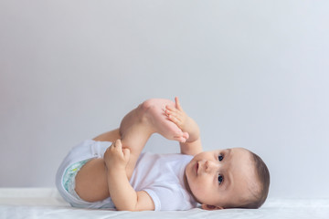 Little hungry baby boy taking feet in mouth. 6-month baby having fun in white bedding. Cute baby...