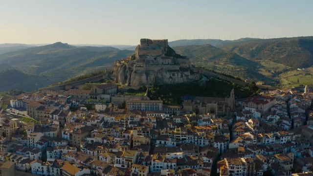Sun behind mountain of Morella. The city with castle, old houses and fortified walls as foreground, sunset as background. Valencia, Spain.