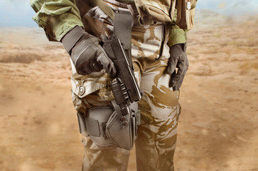 Military soldier woman in camouflage pants and holster holding a pistol on desert background.
