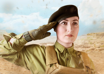Portrait of young beautiful military soldier woman in military beret saluting on desert background. 