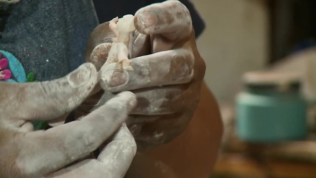 A hand held close up shot of a person adding arms to a  human figure made from dough with the focus being on the hands covered in powder.