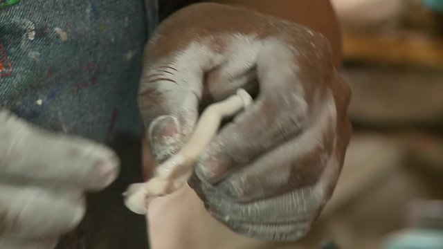 A hand held close up shot of a person adding arms to a  human figure made from dough with the focus being on the hands covered in powder.