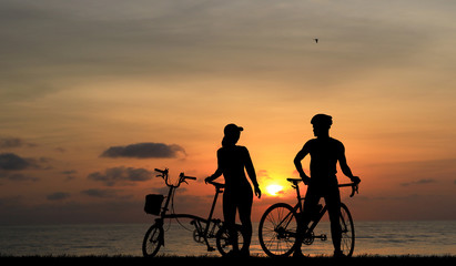 Obraz na płótnie Canvas Silhouette couple and bike relaxing on blurry sunset background.