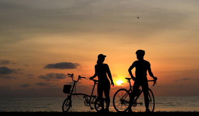 Obraz premium Silhouette couple and bike relaxing on blurry sunset background.