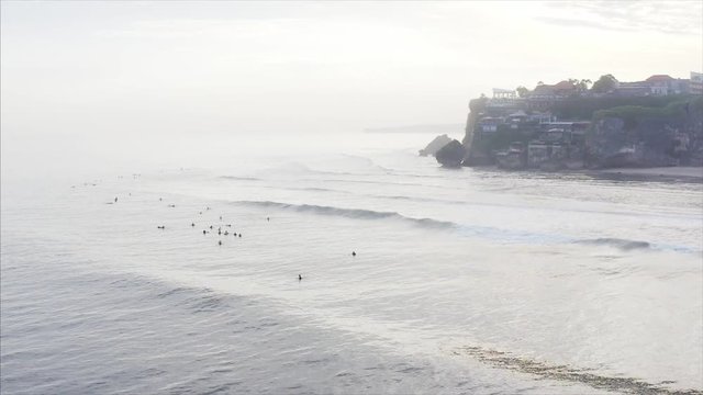 Aerial view of famous Uluwatu spot and surfers waving on Indian ocean waves. On the background is cliff with houses, cfes, resorts, etc. Bali, Indonesia