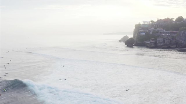Flying above famous Uluwatu spot and surfers waving on Indian ocean waves. On the background is cliff with houses, cfes, resorts, etc. Aerial view. Bali, Indonesia