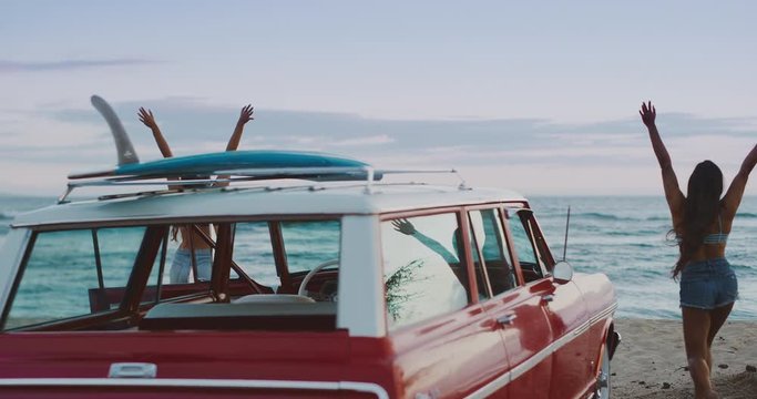 Two friends arriving at the beach in a vintage beach cruiser car to go surfing, two girls getting out of a vintage car at the beach and raising their arms in joy, hawaiian island surf adventure