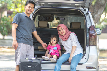 young muslim family , transport, leisure, road trip and people concept - happy man, woman and little girl sitting on trunk of hatchback car and talking outdoors