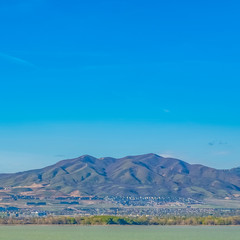 Obraz premium Square Mountain towering over a vast valley and lake under bright blue sky