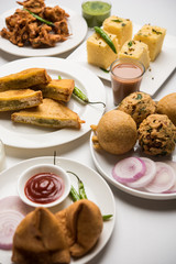 Indian Tea time snacks  in group includes Veg Samosa, Kachori/kachaudi, aloo bonda, khaman dhokla, bread, onion,chilli and moong pakora/pakoda/bhaji/bhajji/Bhajiya/bajji with sauces, selective focus